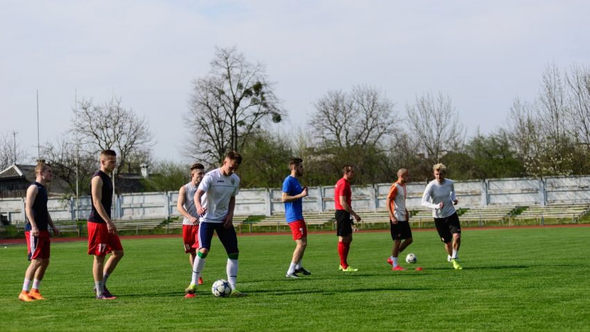 A group of young men practicing football on a lush green field under a bright sky.